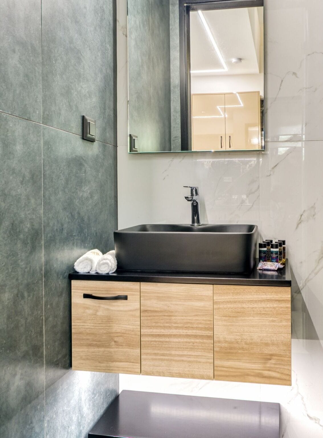 A modern bathroom with a dark sink, wooden cabinets, and a mirror above the sink.