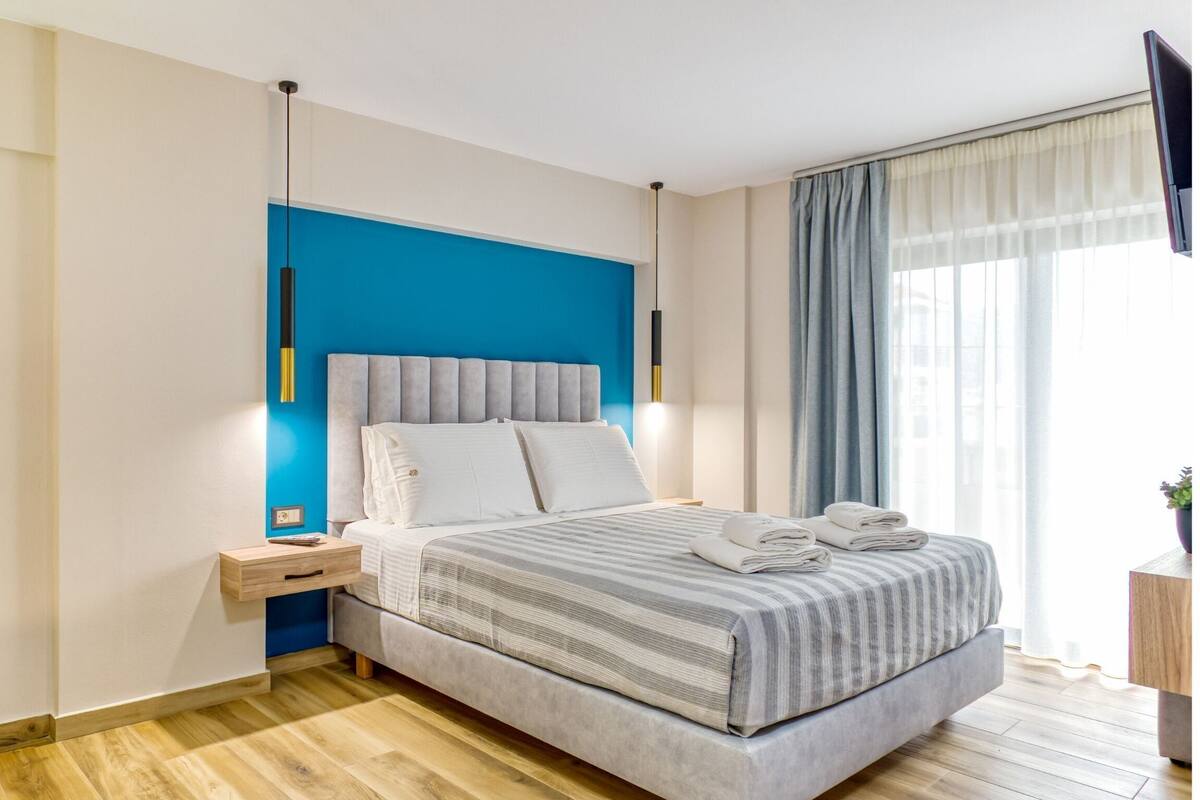 A modern bedroom with a bed, bedside tables, a TV, and a window with curtains.