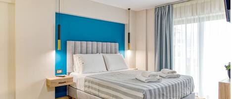 Un dormitorio moderno con cama, mesitas de noche, televisor y ventana con cortinas.