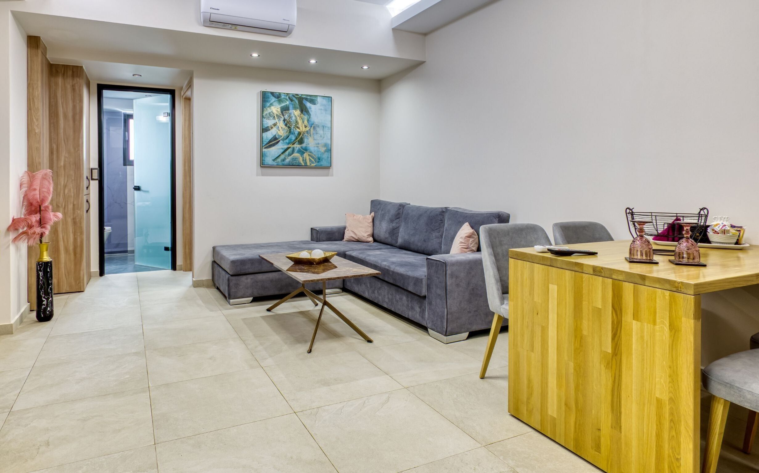 Ein modernes Wohnzimmer mit einem grauen Ecksofa, einem Holzessttisch und einer Glastür zu einem weiteren Raum.