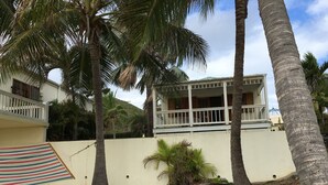 Una propiedad frente a la playa con un edificio blanco, palmeras y un paraguas de playa a rayas.