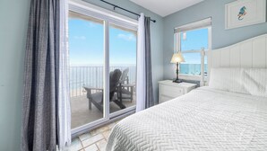 Ein Schlafzimmer mit einem großen Bett, einem Nachttisch, einer Lampe und Blick auf den Strand durch eine Glastür.