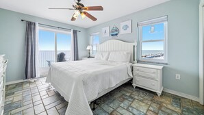 Ein Schlafzimmer mit Bett, Nachttisch, Deckenventilator, Fenster mit Blick und Fliesenboden.