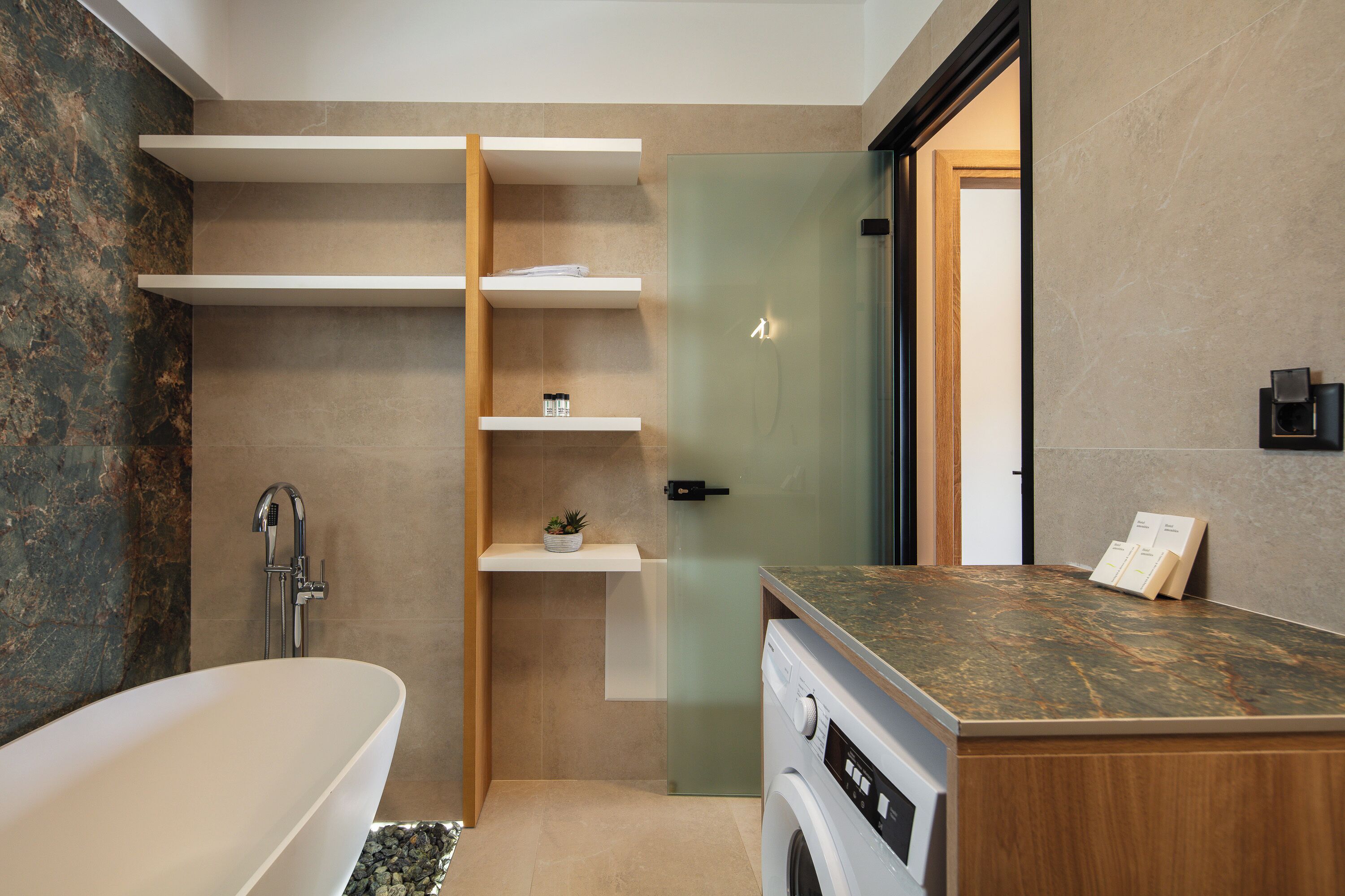 Une salle de bain moderne avec une baignoire sur pieds, des étagères intégrées, un lave-linge et une cabine de douche en verre.