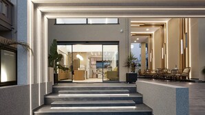 A modern hotel lobby with a staircase leading to the entrance, a seating area with wicker furniture, and a view of the interior through the glass doors. - Sapphire Horizon Suites (Kissamos)