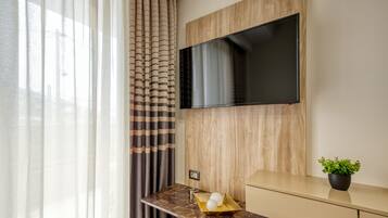 Una habitación moderna con una televisión de pantalla plana en una pared de madera, una encimera de mármol con una planta y una ventana con cortinas traslúcidas.
