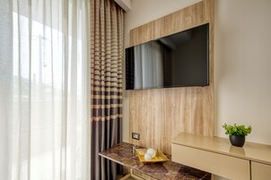 Una habitación moderna con una televisión de pantalla plana en una pared de madera, una encimera de mármol con una planta y una ventana con cortinas traslúcidas.