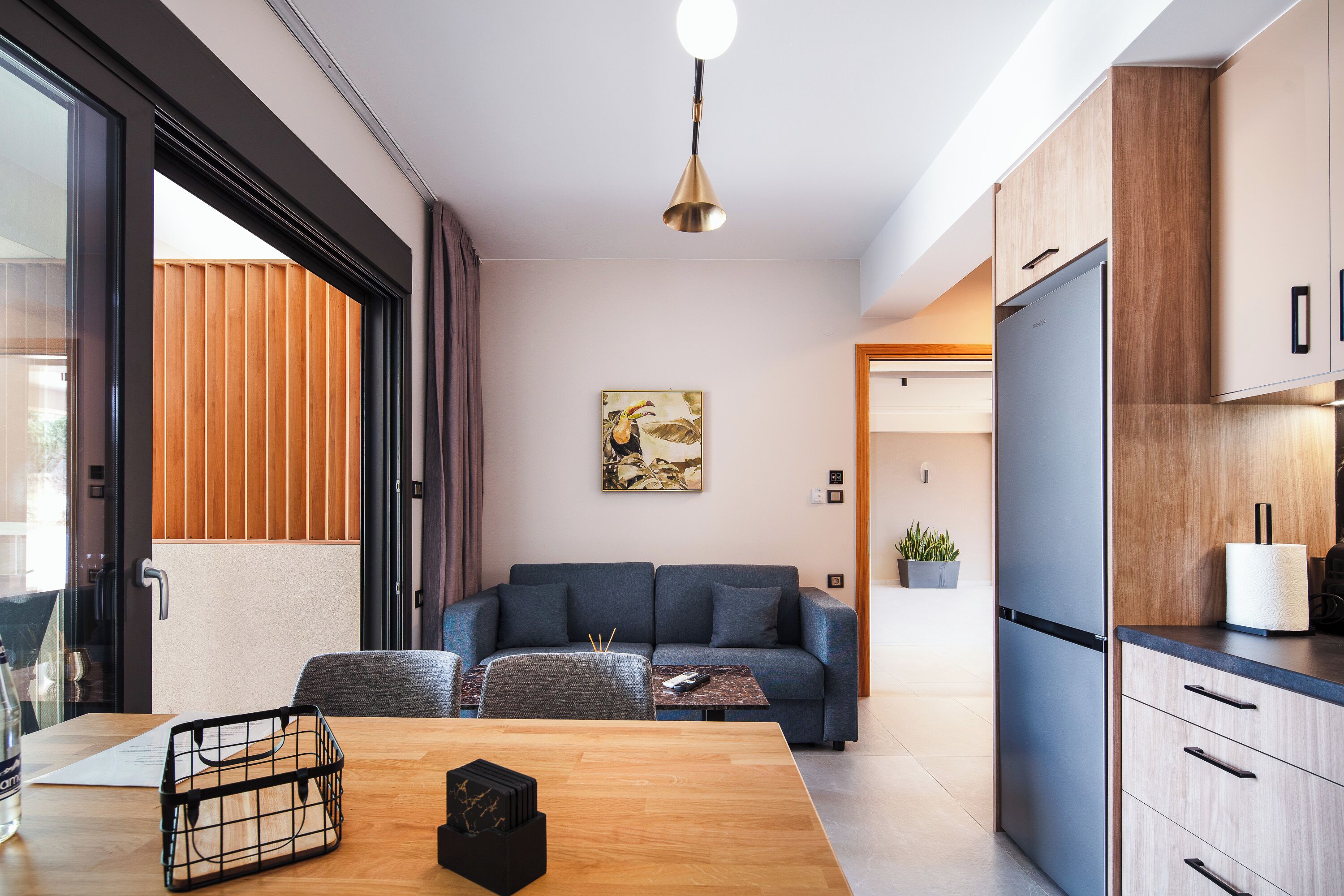 A modern kitchen with a dining area, a sofa, and a large window.