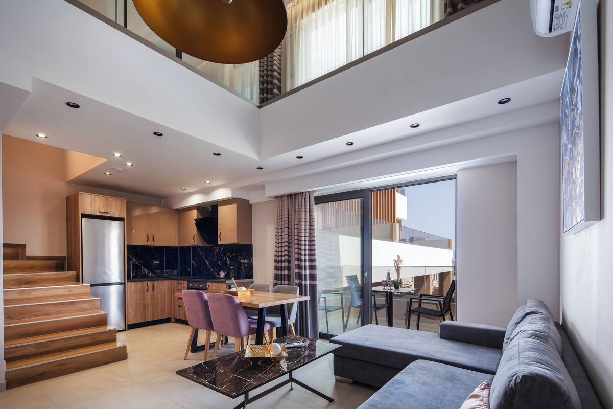 A modern living space with a staircase, dining area, kitchen, and a balcony with a view.