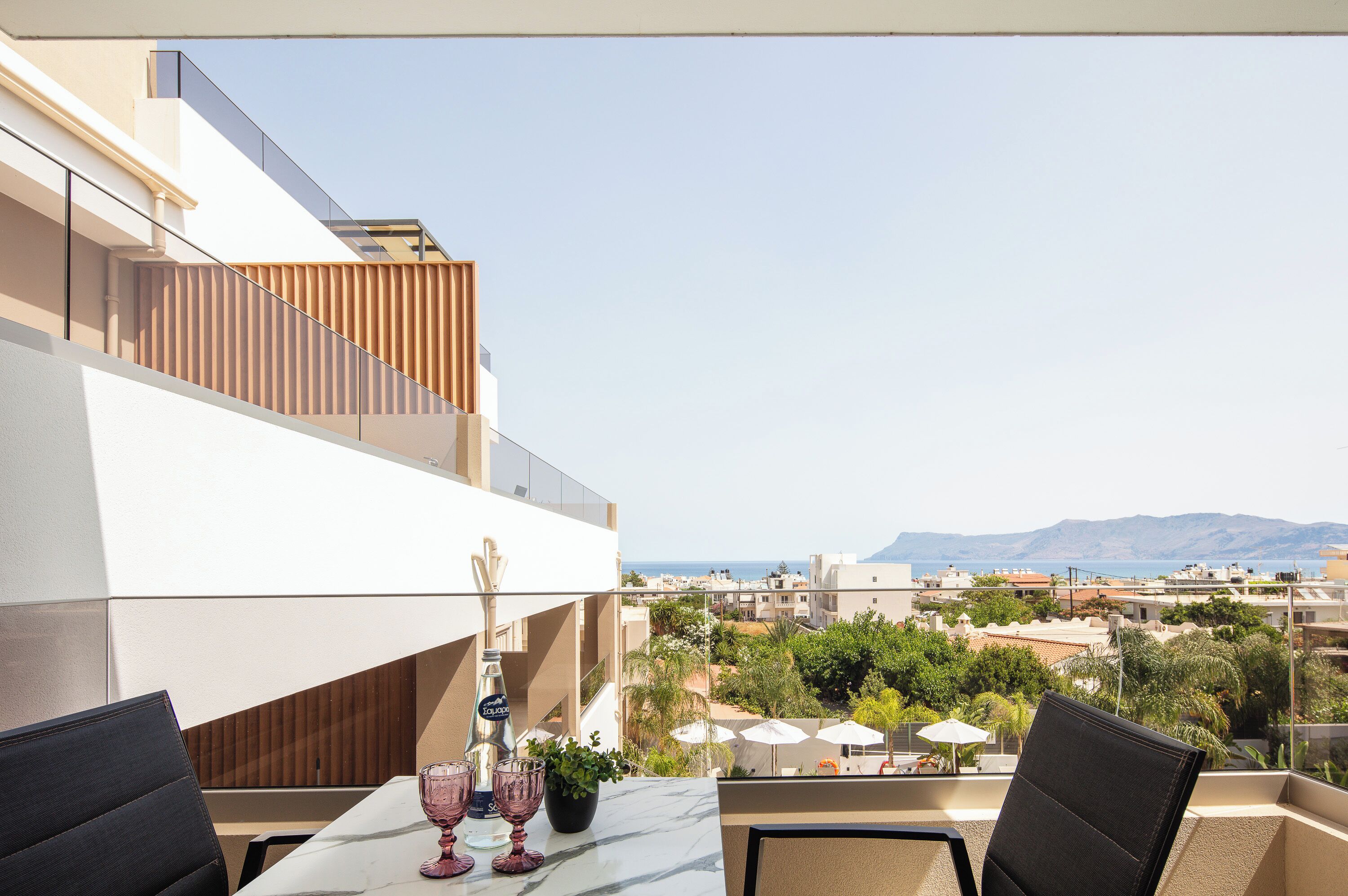 A balcony with a table, chairs, and a bottle of champagne. The view includes a cityscape and mountains.
