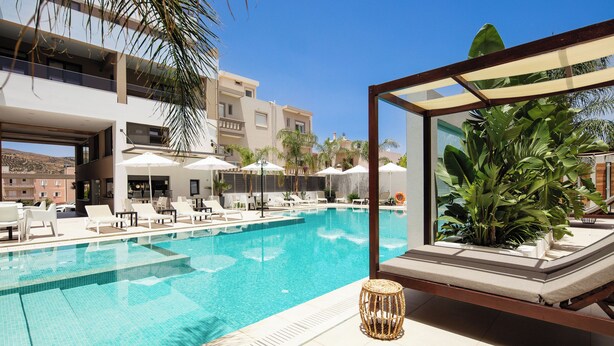 A swimming pool with lounge chairs and umbrellas, surrounded by palm trees and a modern building. - Sapphire Horizon Suites (Kissamos)
