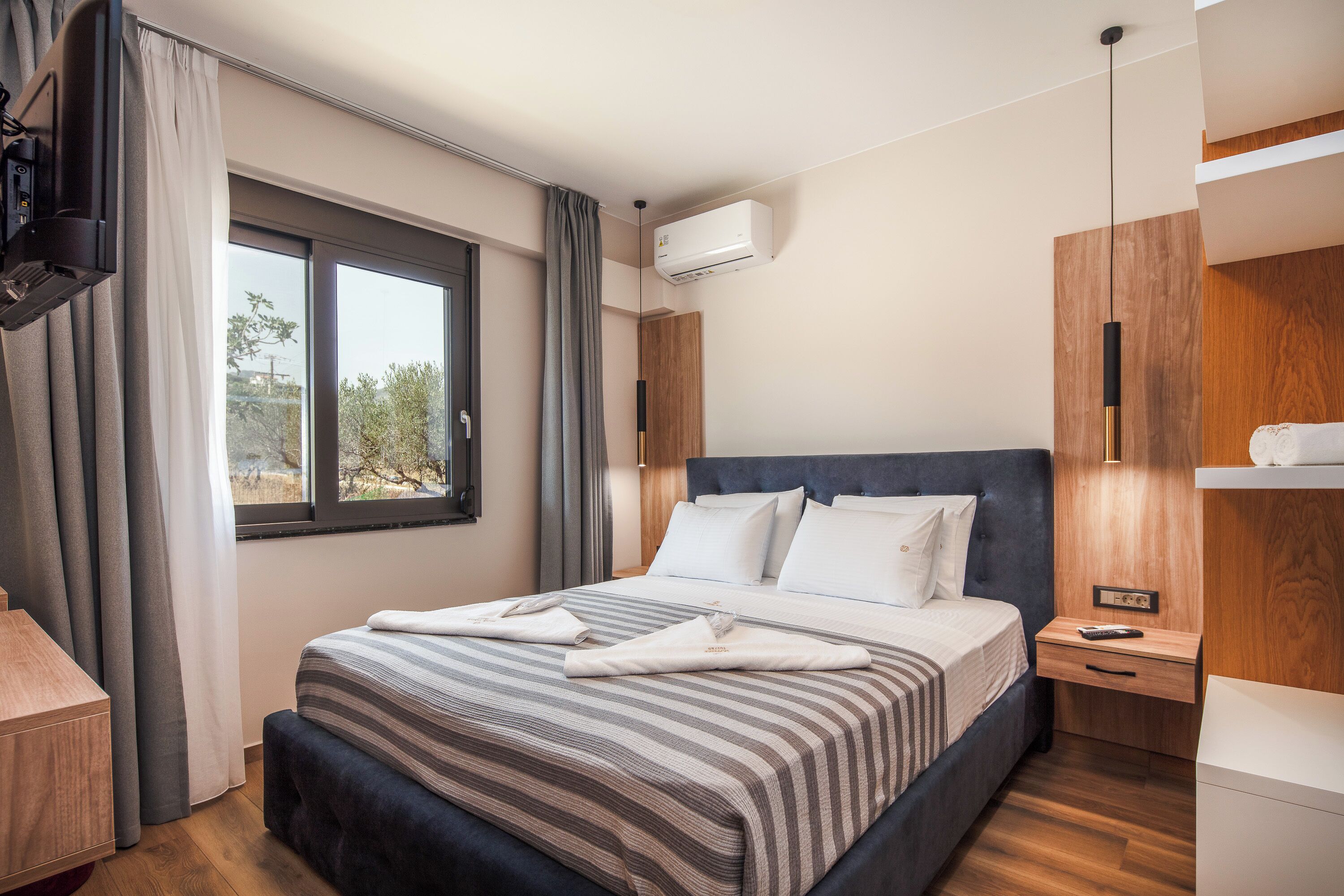 A modern hotel room with a large bed, a bedside table, a nightstand, an air conditioning unit, and a window with curtains.