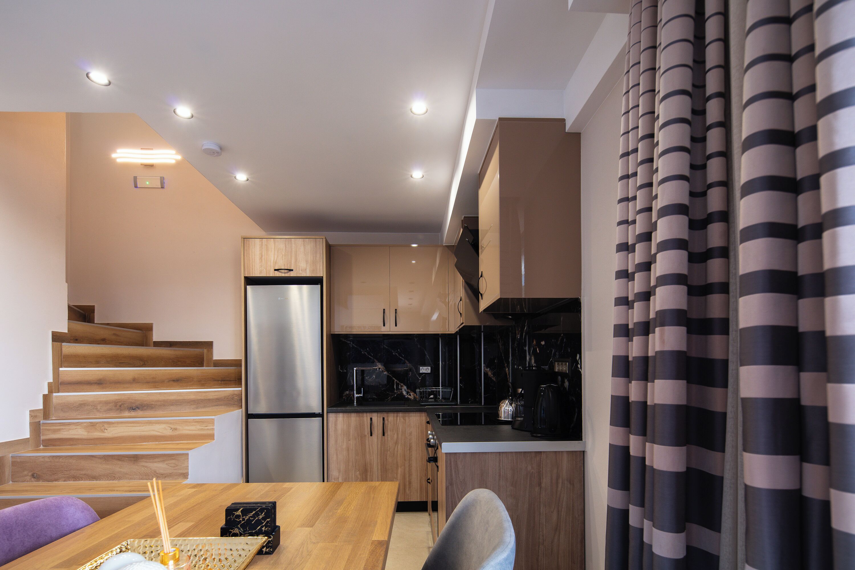 A modern kitchen with wooden cabinets, a stainless steel refrigerator, and a marble countertop.
