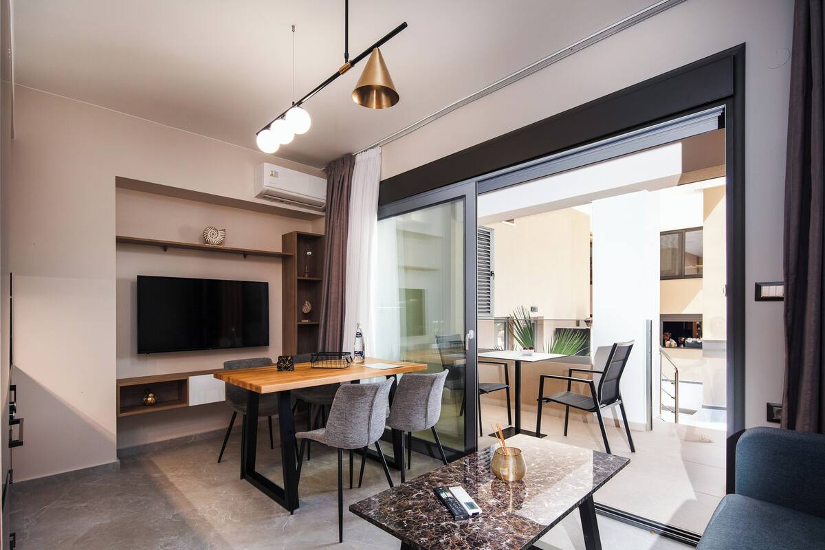 A modern living room with a flat-screen TV, a wooden dining table, and comfortable seating.