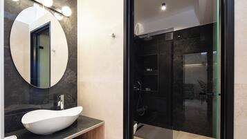 Une salle de bain moderne avec un grand miroir rond, un lavabo sur colonne blanc et une douche à l’italienne.