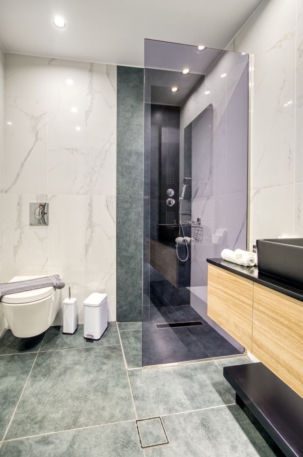 A modern bathroom with a glass-enclosed shower, a toilet, a bidet, and a vanity with a towel.