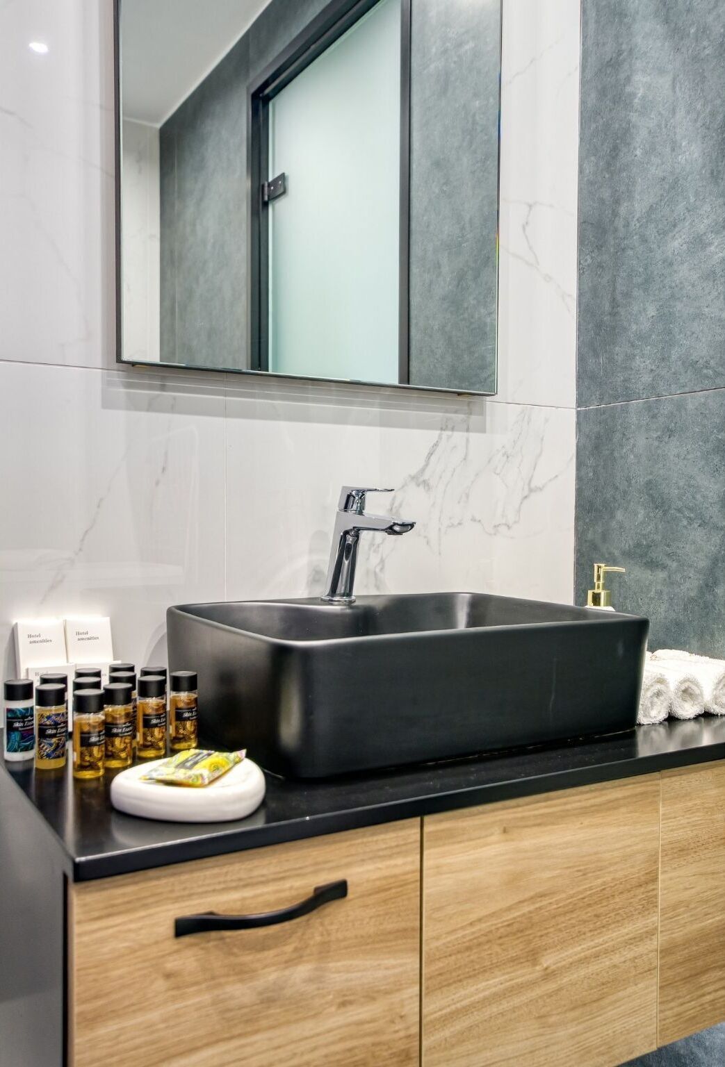 A modern bathroom with a black sink, marble walls, and a mirror above it. There are toiletries on the counter.