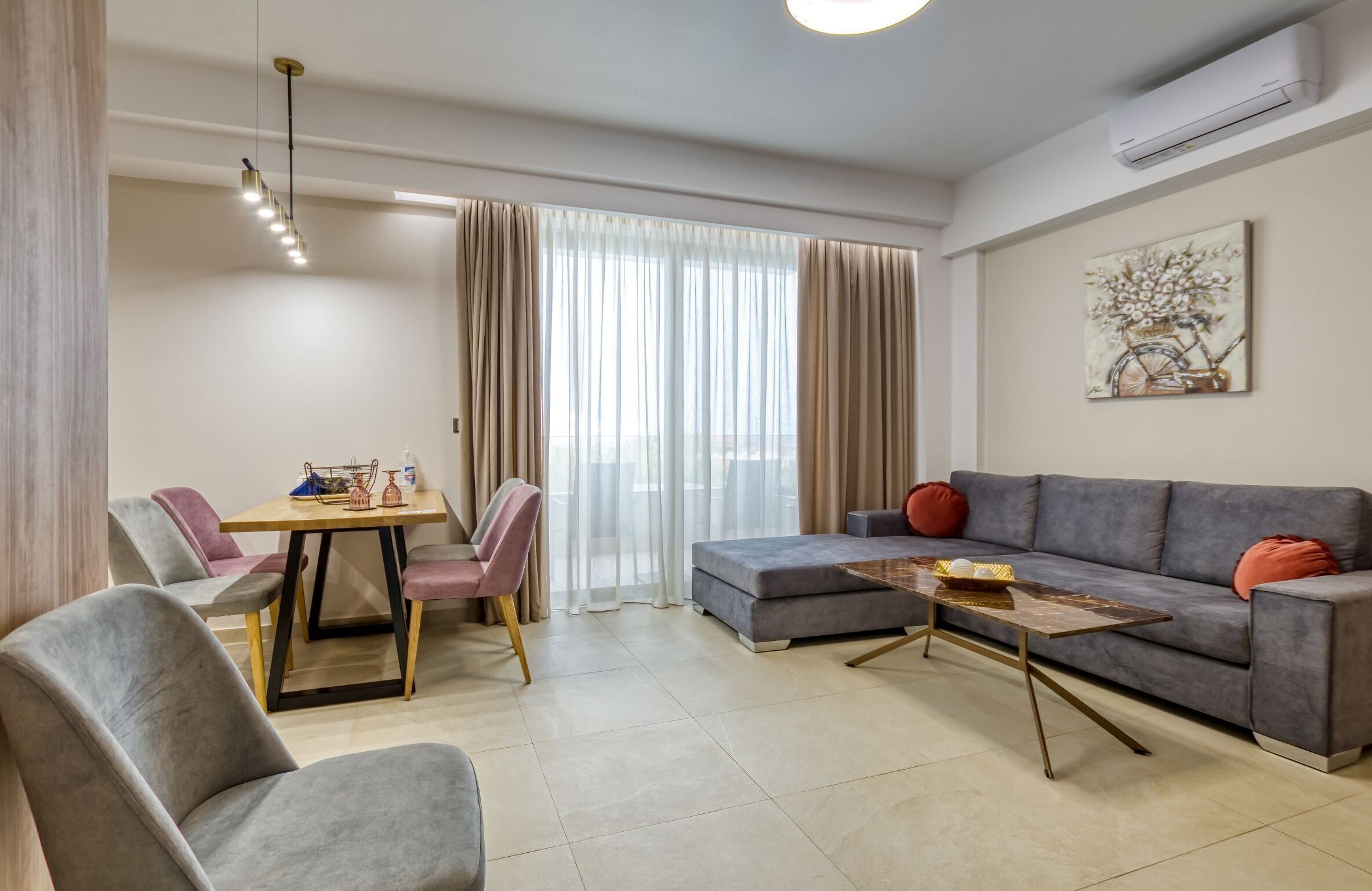 A modern living room with a grey sofa, a wooden coffee table, and a dining area with a table and chairs.