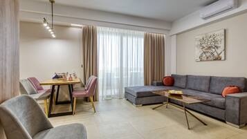 A modern living room with a grey sofa, a wooden coffee table, and a dining area with a table and chairs.