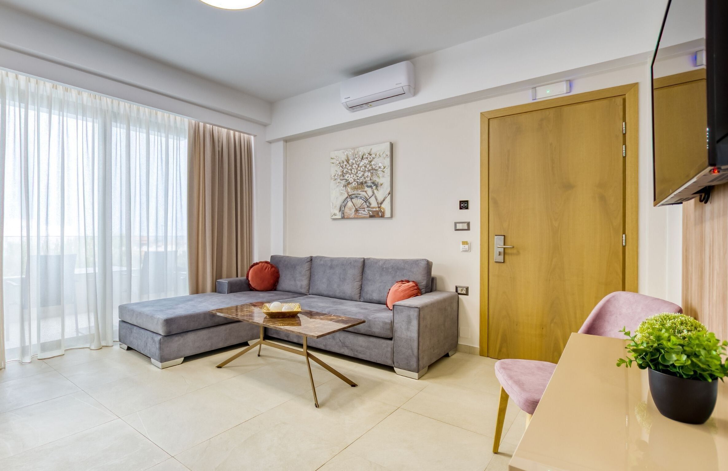 Una sala de estar moderna con un sofá gris, una mesa de centro, un televisor montado en la pared y una puerta de madera.
