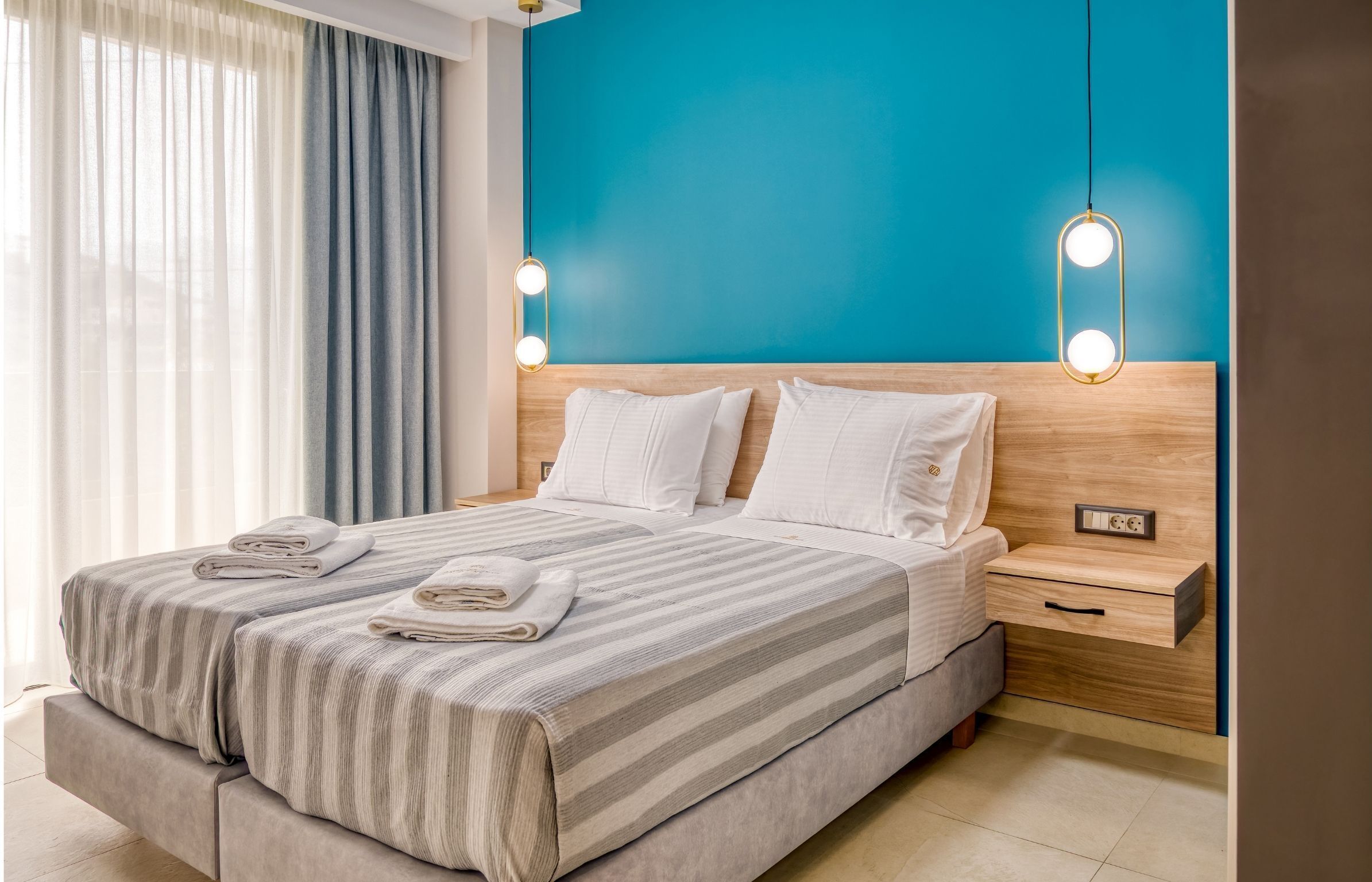 A modern hotel room with a large bed, a wooden headboard, and a blue accent wall.
