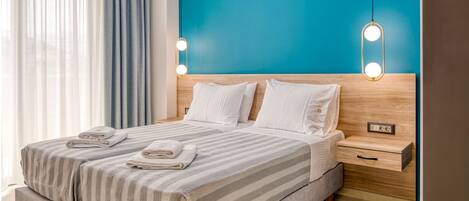 A modern hotel room with a large bed, a wooden headboard, and a blue accent wall.