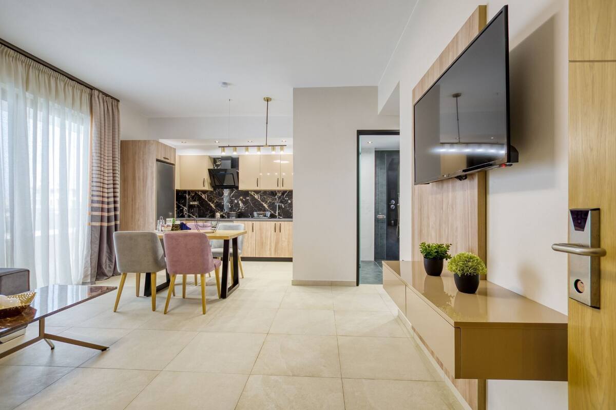 A modern living room with a TV, a dining area, and a kitchen in the background.
