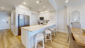 A modern kitchen with white cabinetry, a stainless steel refrigerator, a microwave, and a large island with stools. - Tides 405 ~ Amazing gulf-front view ~ Huge private balcony (Miramar Beach)