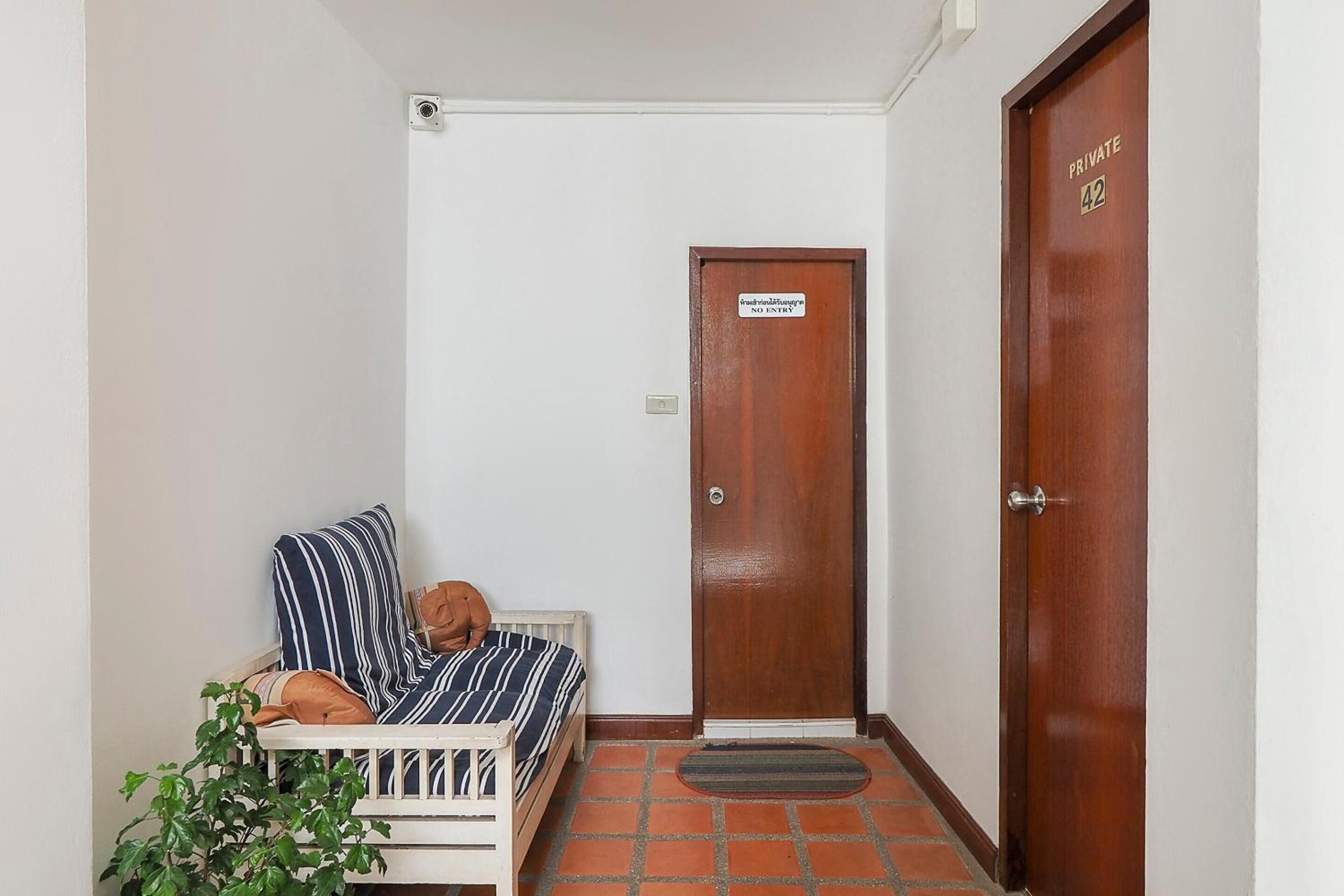 Una habitación pequeña con una cama, una puerta con la etiqueta “PRIVATE 42” y un felpudo.