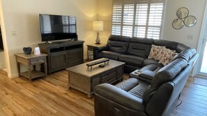 Una sala de estar con un sofá modular, un televisor de pantalla plana, una mesa de centro y una lámpara.