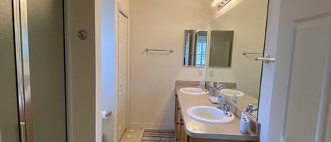 A modern bathroom with two sinks, a mirror, and a shower.