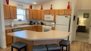 Una cocina moderna con armarios de madera, una isla central con taburetes, microondas, estufa y refrigerador.