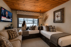 A cozy room with a large window, a television displaying news, and a framed artwork on the wall.