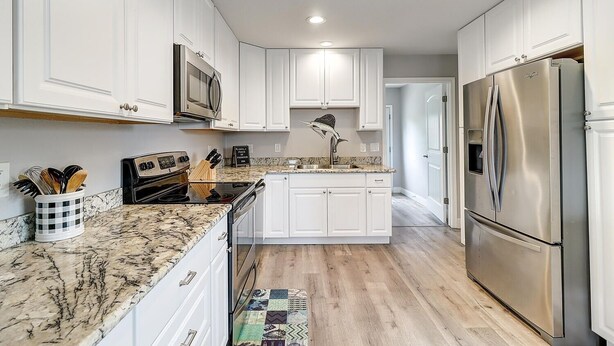 A modern kitchen with white cabinets, stainless steel appliances, and a granite countertop.