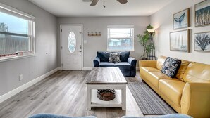 A living room with a ceiling fan, a coffee table, a sofa, and a couch. There are windows with blinds, a door with a glass panel, and a plant.