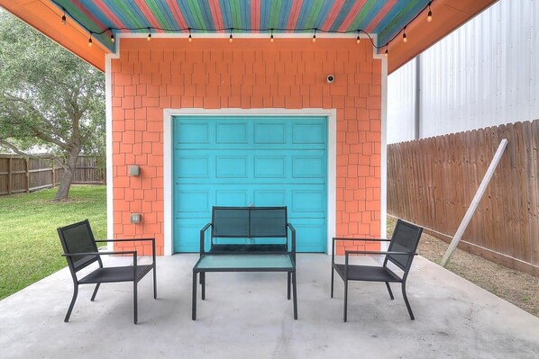 Un patio con una puerta de garaje turquesa, paredes de ladrillo y dos sillas de metal negro.
