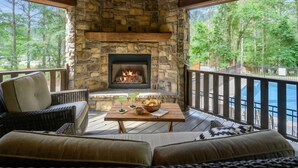 A stone fireplace with a fire, a wooden deck, outdoor furniture, and a view of a body of water.