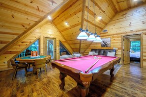 Un intérieur en bois agrémenté d’une table de billard, d’une table de jeu de flipper et d’un coin salon confortable.