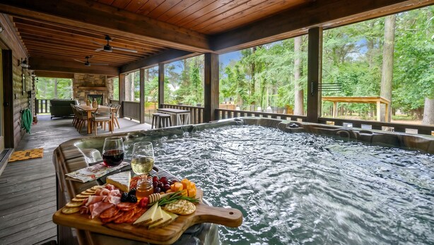 A hot tub with a wooden deck, surrounded by a wooden deck and large windows with a view of trees.