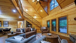 A log cabin interior with a staircase, wooden walls, and a living area with sofas and a coffee table.