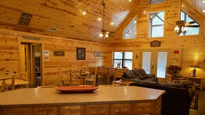 L’intérieur d’une cabane en rondins comprend un coin cuisine, une table à manger et une cheminée.