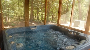 Un bain à remous avec vue sur une forêt, visible à travers des fenêtres à cadre en bois.