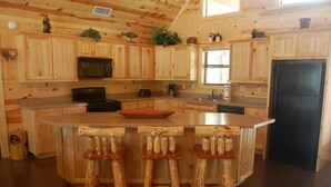 Une cuisine de style rustique, avec des éléments en bois, comprenant un îlot central, des tabourets de bar, un four à micro-ondes et un réfrigérateur.