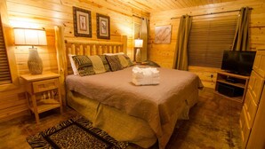 Un dormitorio rústico de madera con una cama grande, paredes de madera, un televisor y cuadros enmarcados.