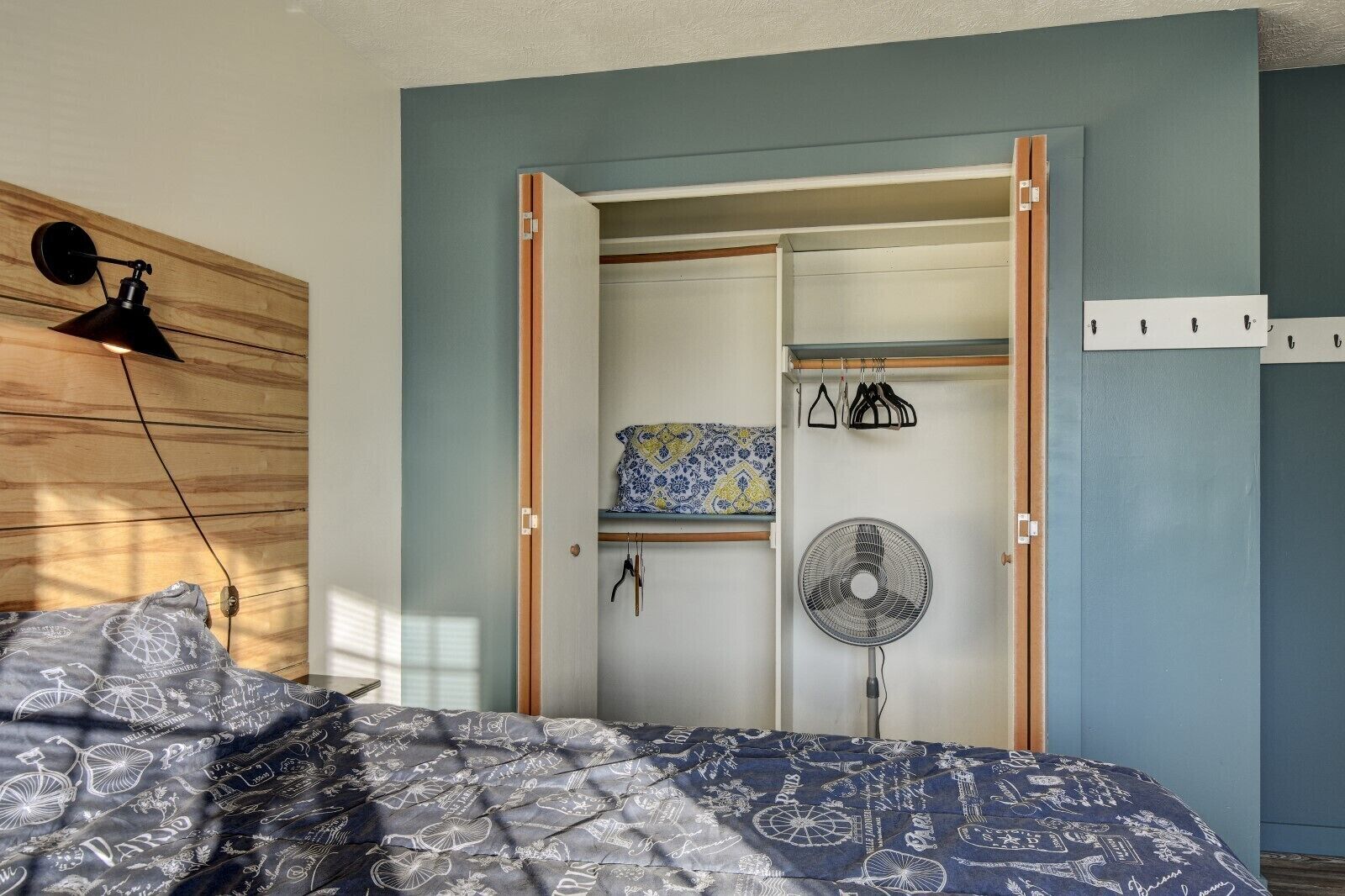 Une chambre à coucher comprenant un lit, une armoire, un ventilateur et une lampe fixée au mur.