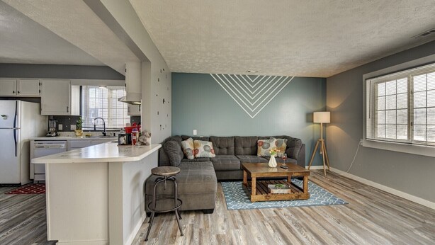 Una cocina moderna con armarios blancos, una isla central y un área de comedor con sofá y mesa de centro.