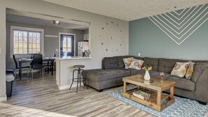 Una sala de estar moderna con un sofá gris, una mesa de centro de madera y un comedor con una puerta azul.