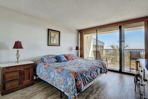 A bedroom with a large bed, wooden dresser, and a balcony with a view.