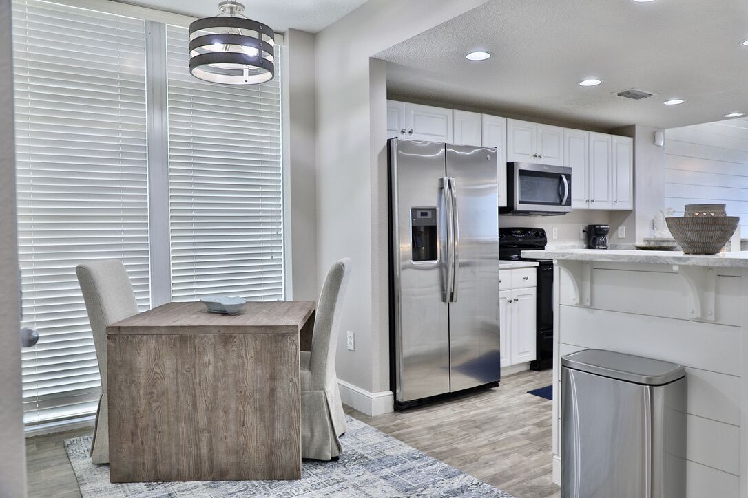 A modern kitchen with white cabinets, stainless steel appliances, and a dining area with a wooden table and chairs.