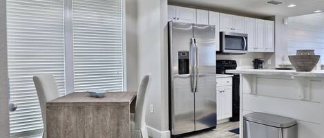 A modern kitchen with white cabinets, stainless steel appliances, and a dining area with a wooden table and chairs.